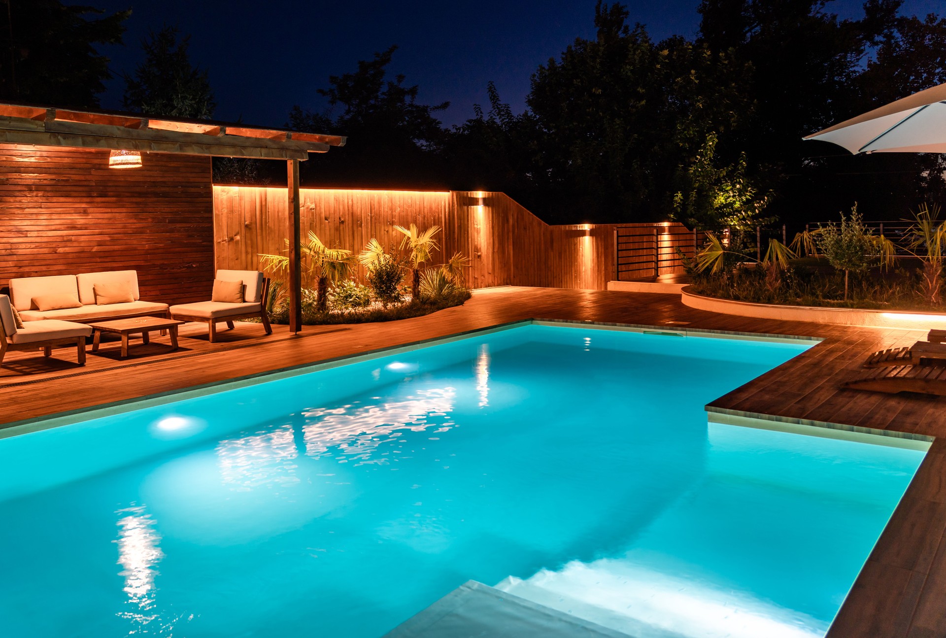 Modern pool with soft lighting, wooden deck, and loungers at night. Concept of peaceful outdoor escape